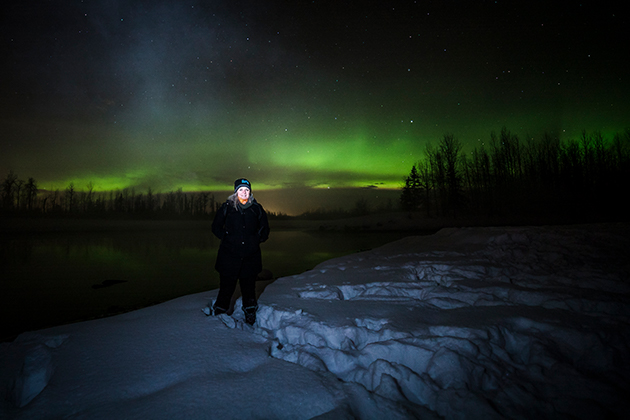A woman standing on a snow covered hill next to a lake under a green light