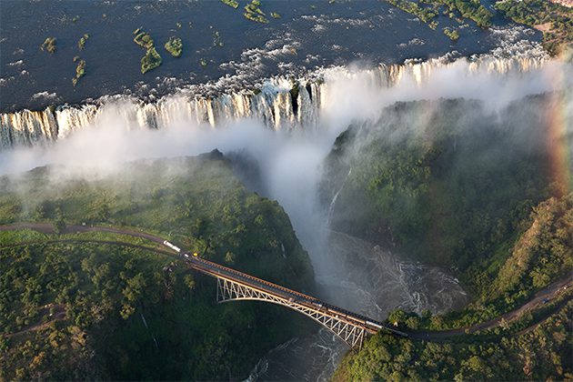 A rainbow over a waterfall and a bridge