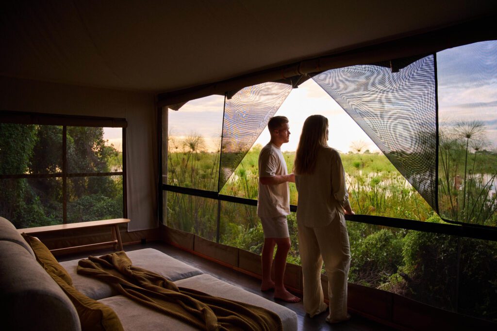 two people looking out of a luxury tent to water and grass