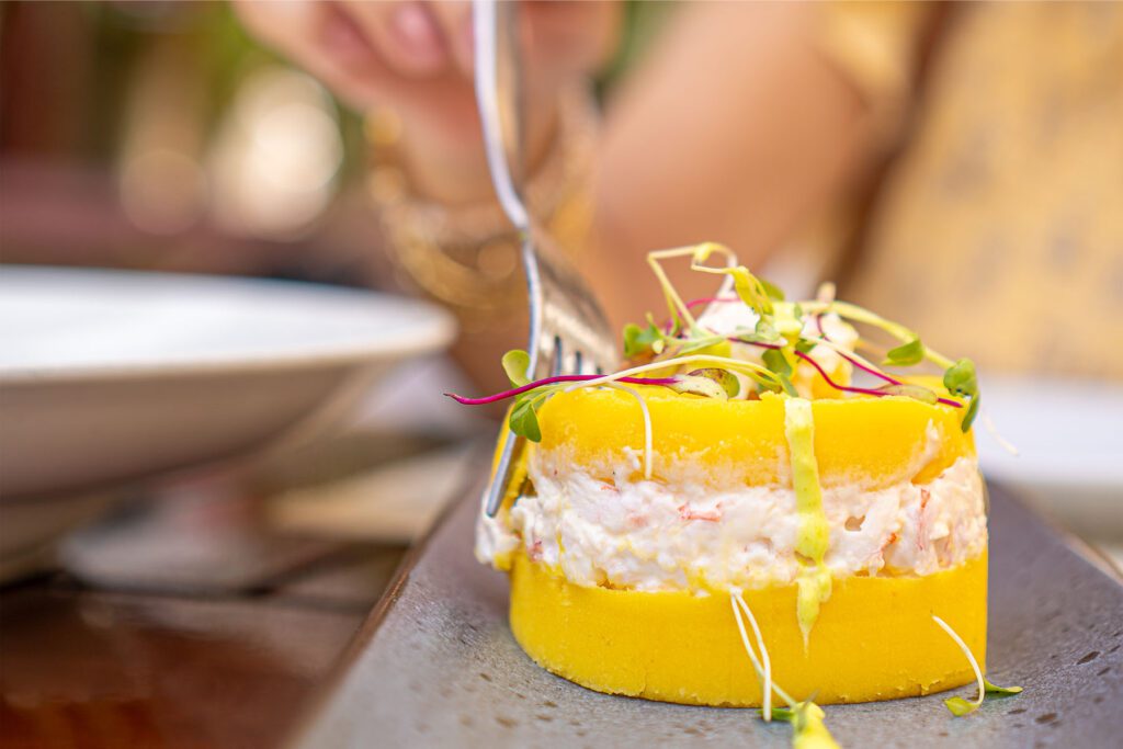 Woman eating causa rellena, peruvian food, with a fork in a restaurant