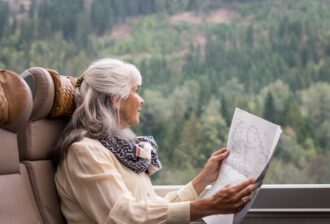 Woman looking out a large window with a paper in hand sitting on a lounge chair