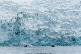 people in an inflatable boats in front of a glacier