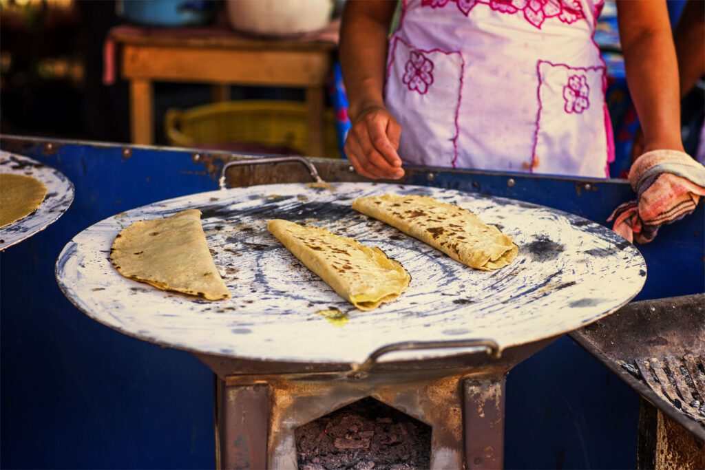 Mexican Quesadillas are tortillas flip filled either with cheese, this is why they are called quesadilla that means chessedillas, but the tortillas might be filled with more things like flor de calabasa, this is pumpkin flower or some other vegetables, the fire stove that we see in the picture is called a comal, the round metal over the fire is the comal this is a special utensil​ to cook Mexican tacos and quesadillas