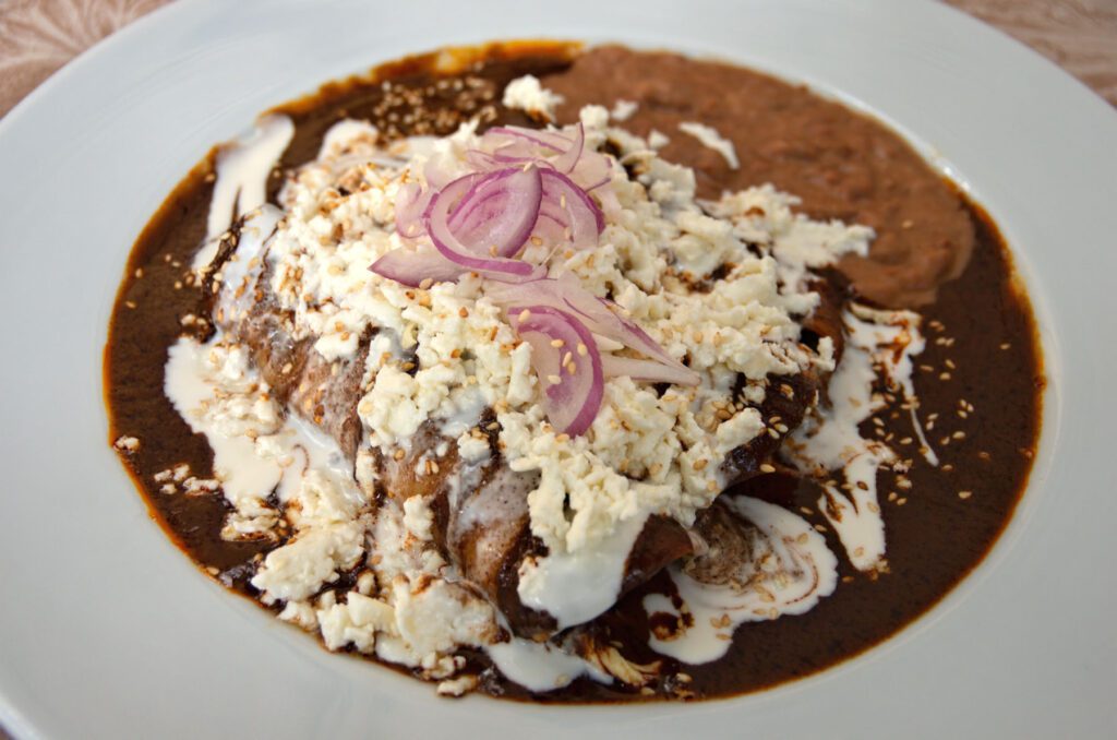 Plate of chicken enmoladas served with cotija cheese, crema and red onion