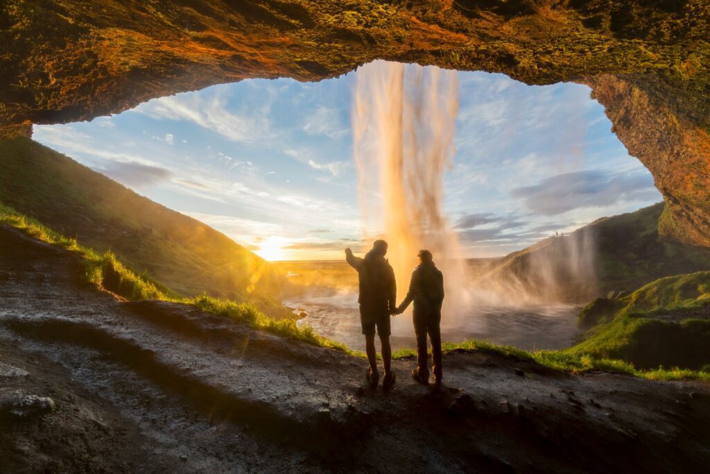 Two people holding hands looking out from behind a waterfall