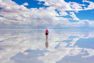 Woman standing in looks like a limitless mirror as the ground reflects the sky