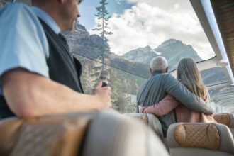 people looking out a glass domed rail carriage at mountains on rocky mountaineer