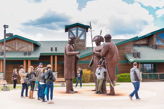 A group of people standing in front of a building with statue of Native Americans
