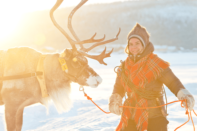 A woman walking a reindeer in the snow