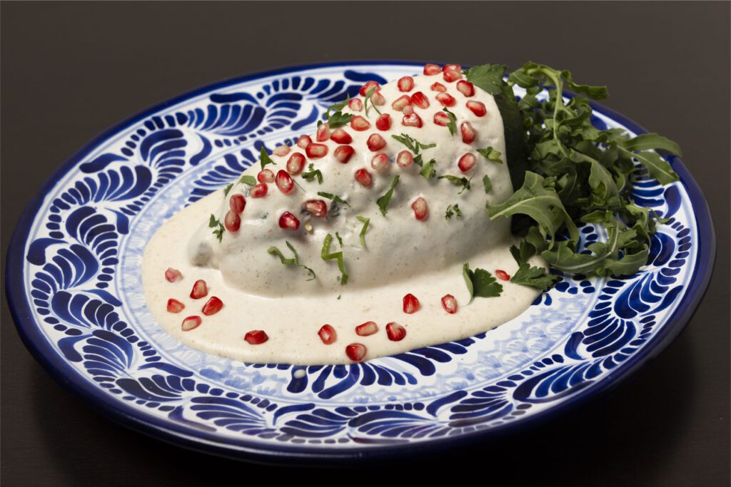 Traditional Mexican food called "Chile en Nogada" which is a poblano pepper, stuffed with beef, pork, chese, apples, peach, nuts and covered with a white nut cream. On top of the cream called "nogada" cilantro and pomegranate grains are placed to represent the colors of the Mexican flag: green, white, and red,