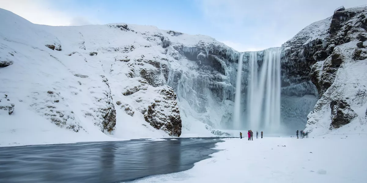 people standing at thge base of a waterfall in winter
