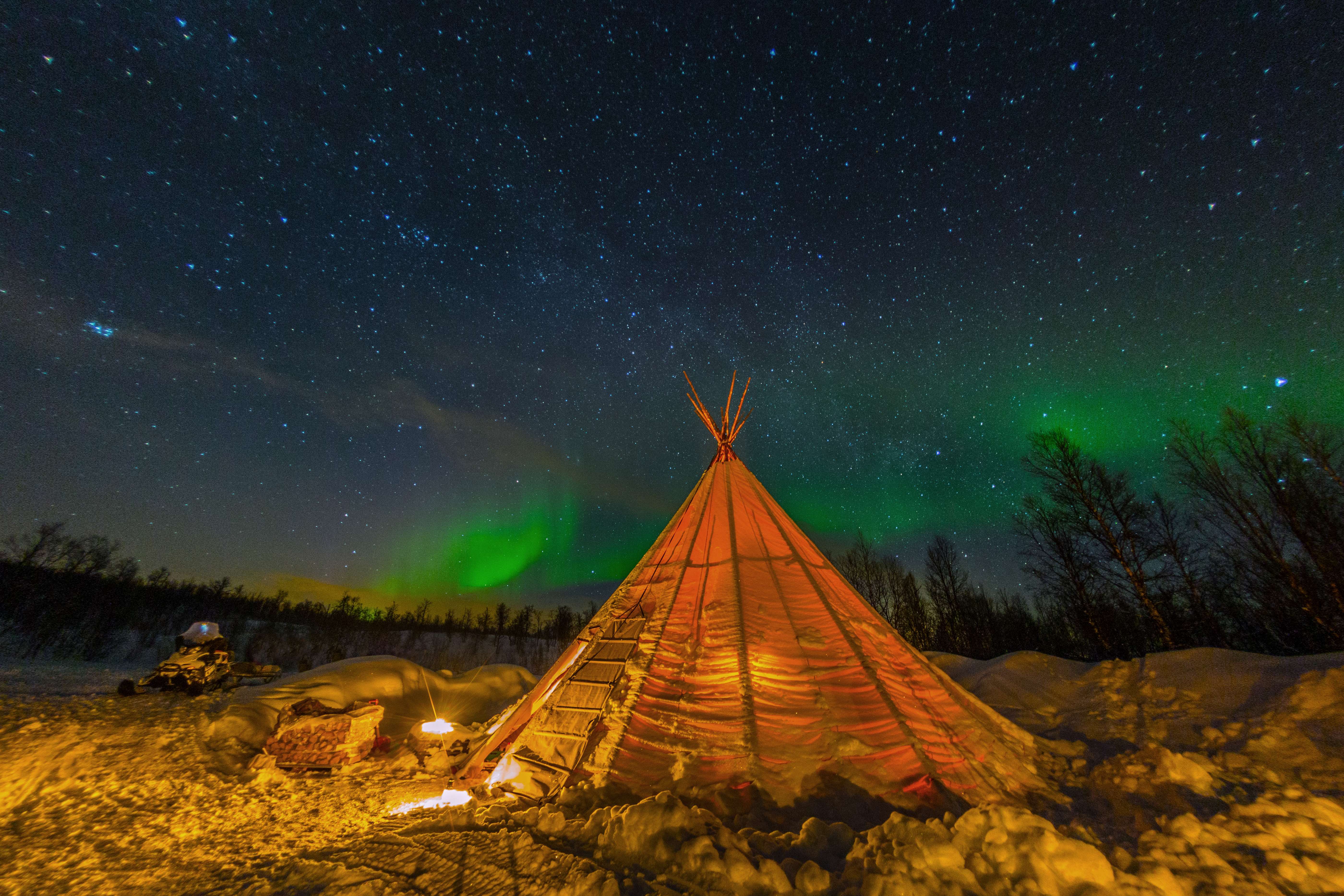 A teepee is lit up in the night sky in Sweden, with the Northern Lights in the skyline