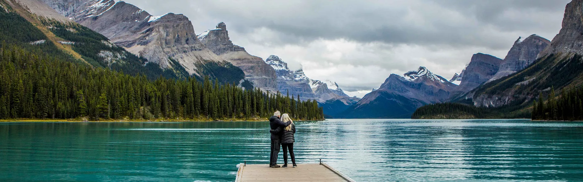 XA couple of people standing on a pier next to Maligne Lake in Canada
