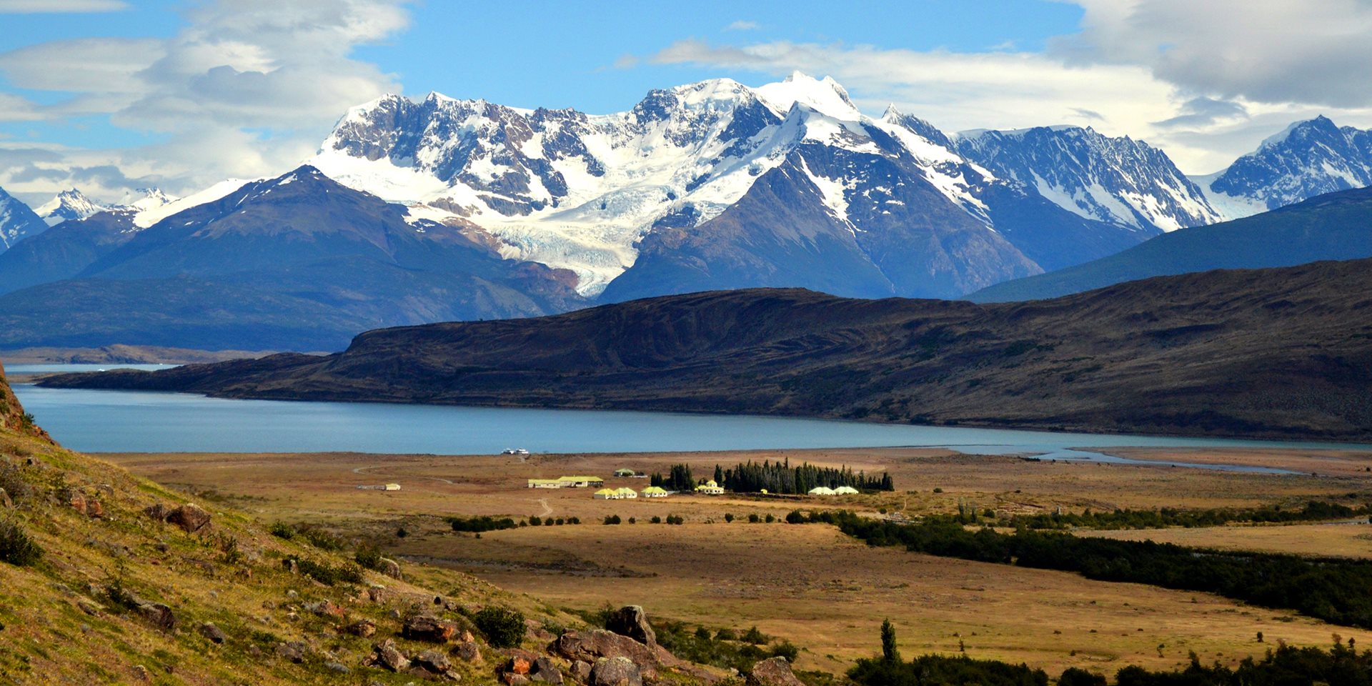 Fields next to a lake with snowy mountains in the background 