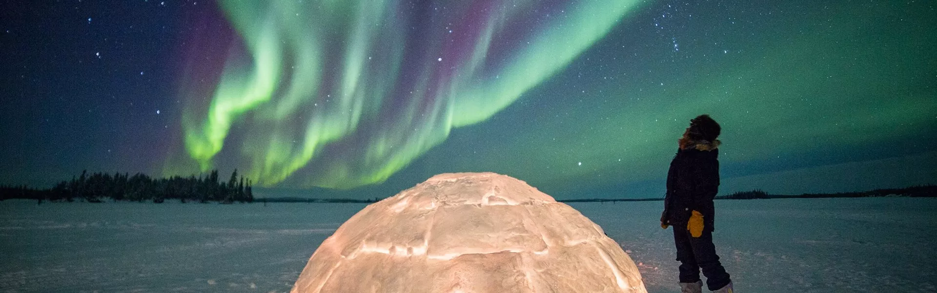 A person standing by an igloo and observing northern lights in Canada