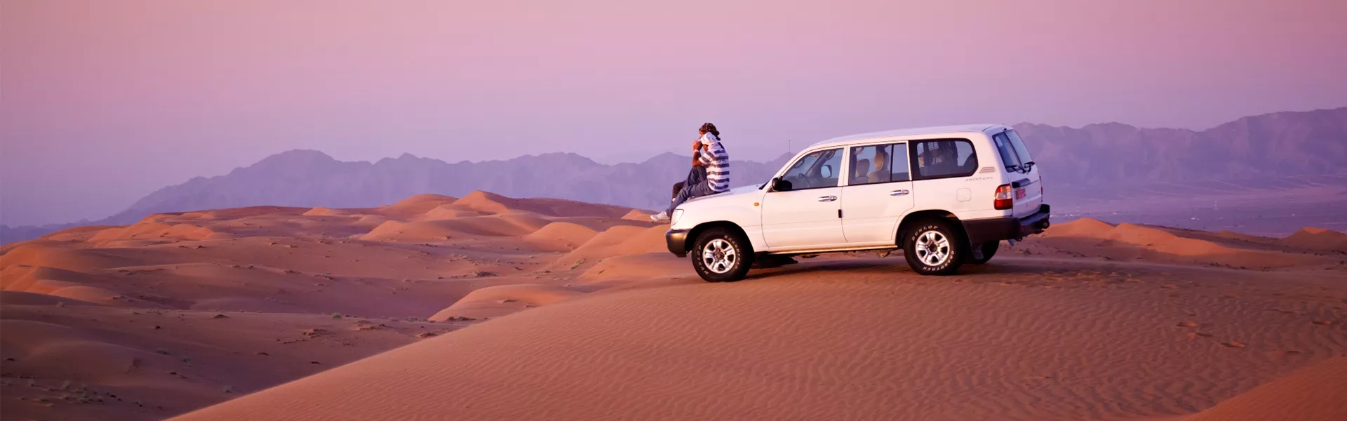 A white suv and people in the middle of a desert