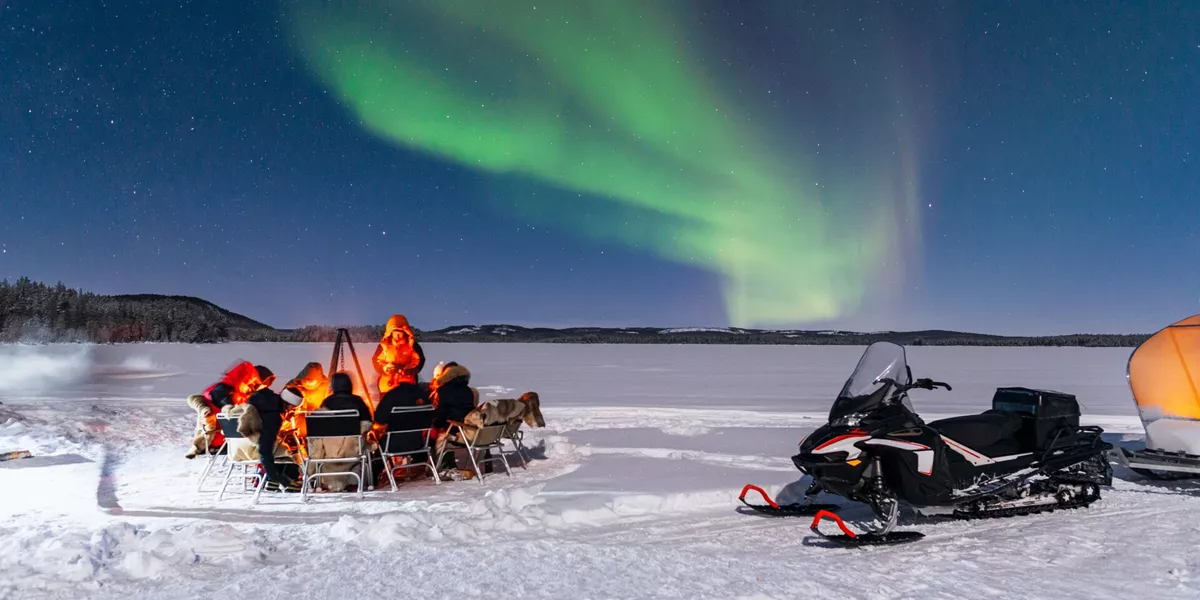 People around a fire with the northern lights above