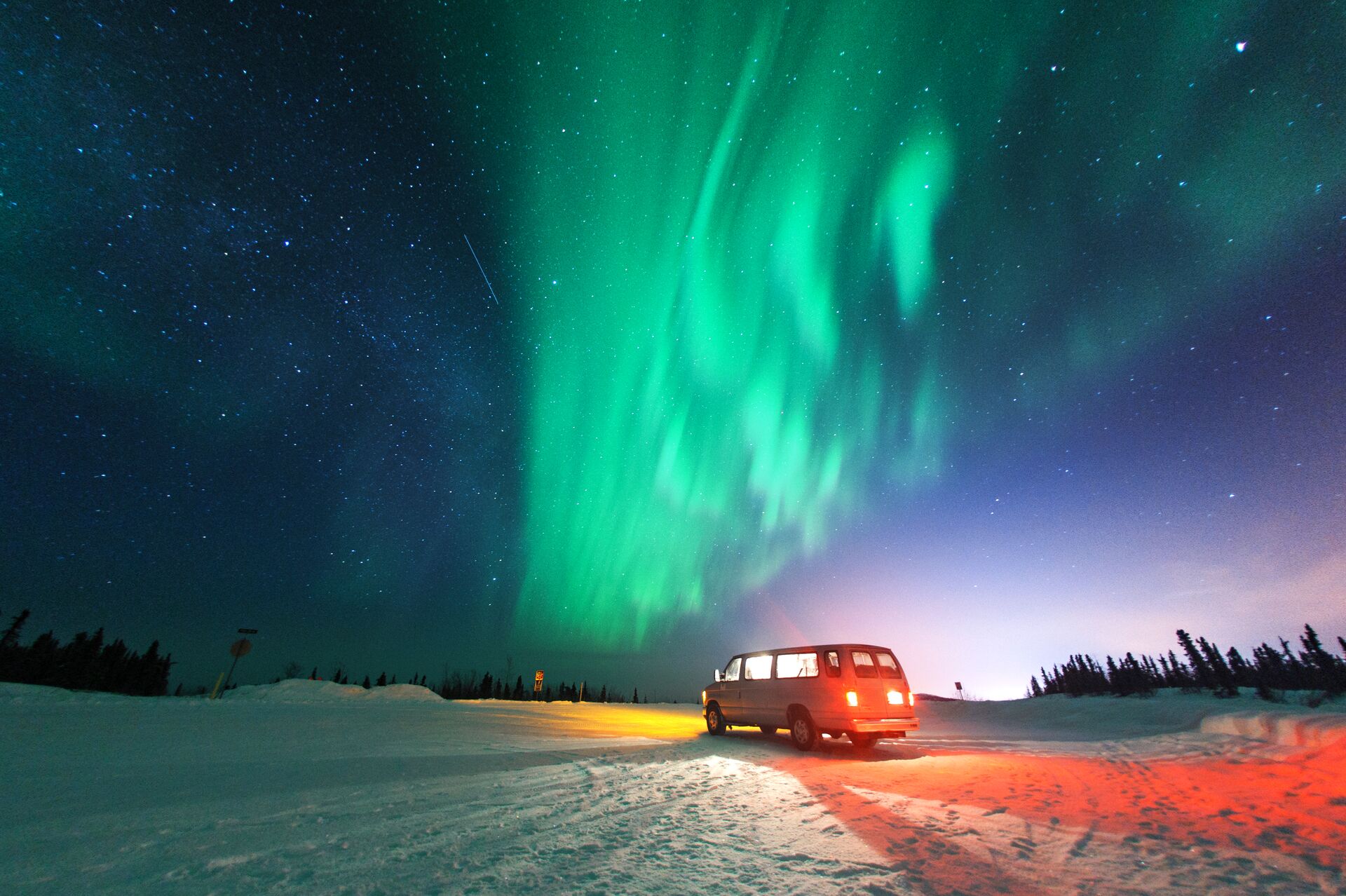 Van parked on a snowy landscape under the northern lights