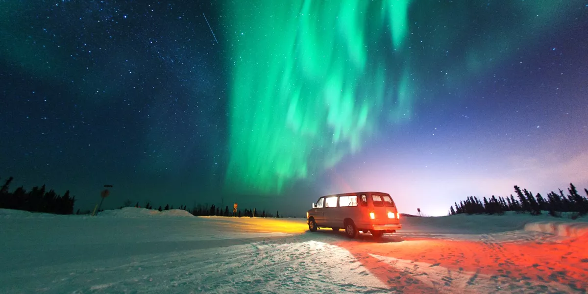 Van parked on a snowy landscape under the northern lights