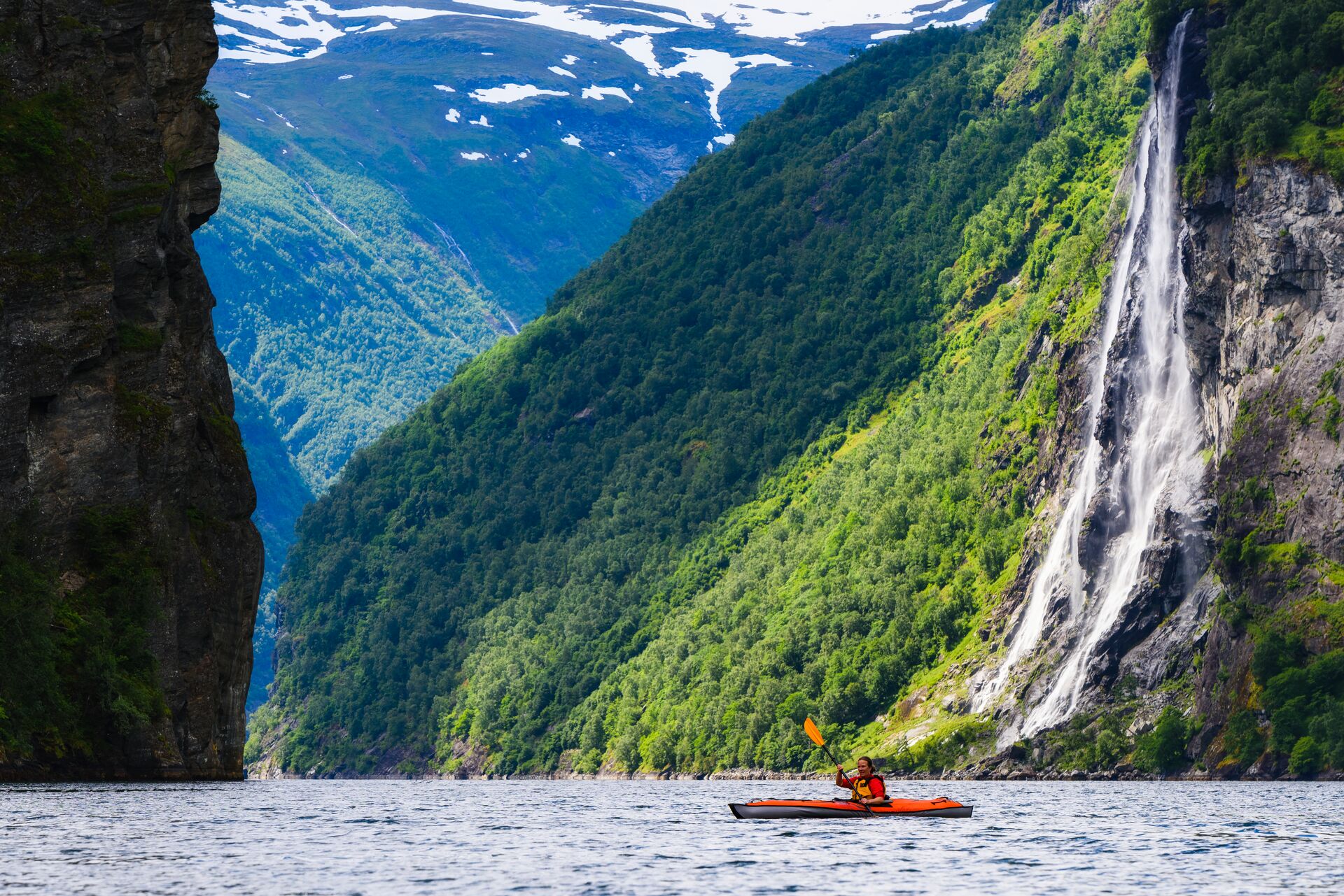 Person Kayaking in a green fjord with a waterfall
