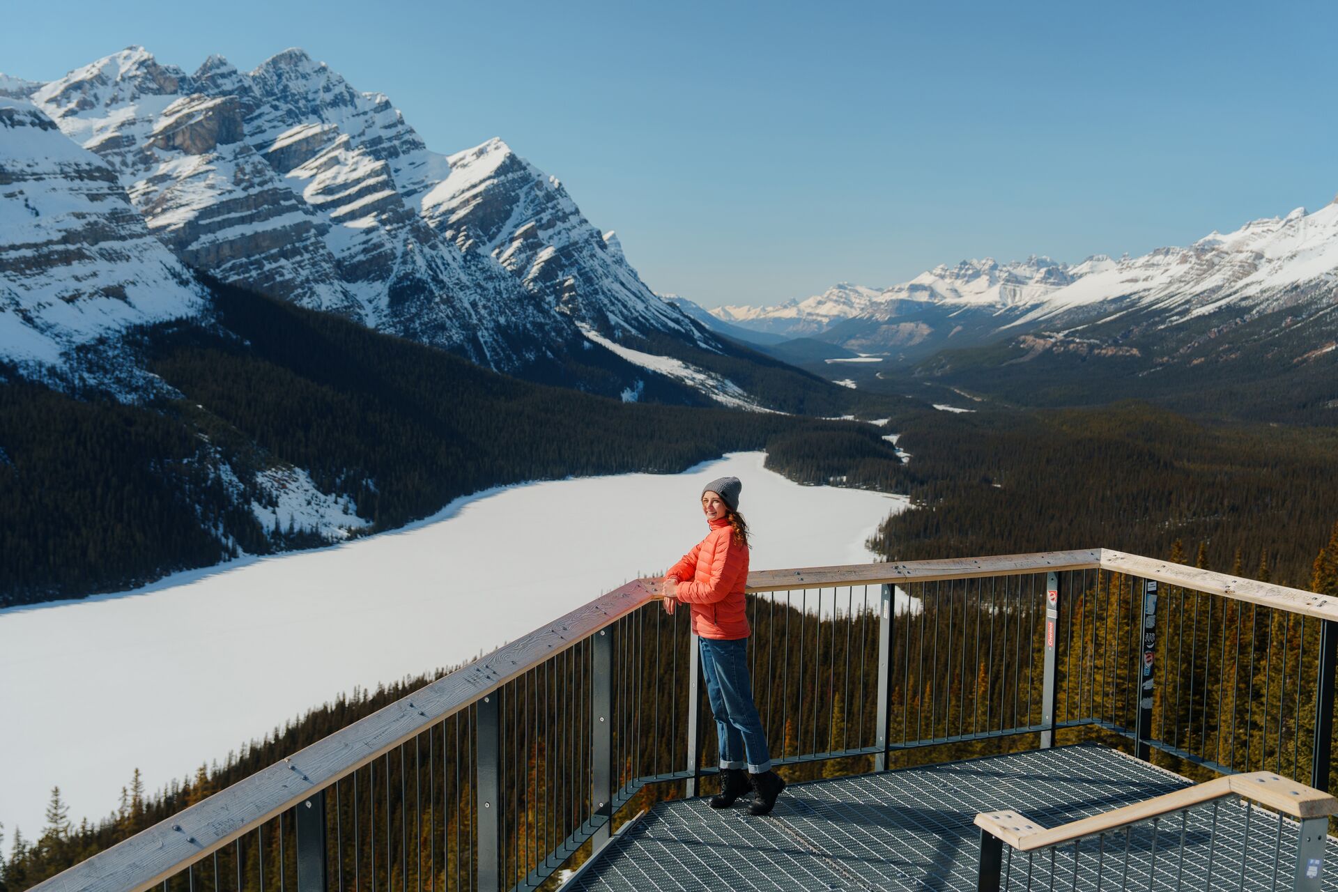 Woman smiling back with frozen lake, forest and mountains in the background