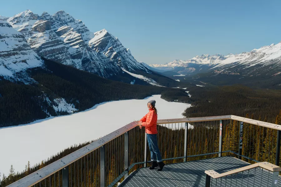 Woman smiling back with frozen lake, forest and mountains in the background