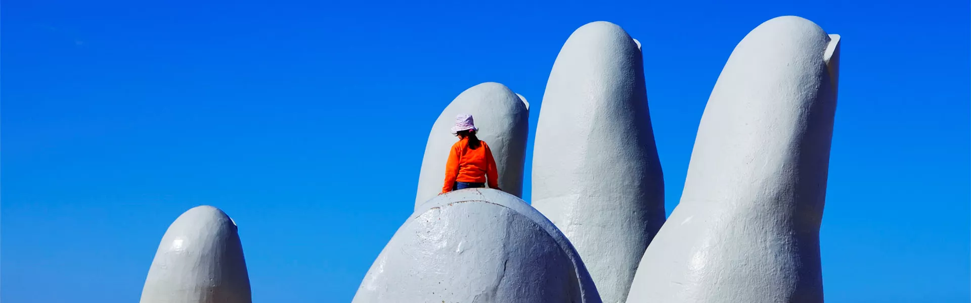 person sitting on a statue of a hand rising out of the sand.