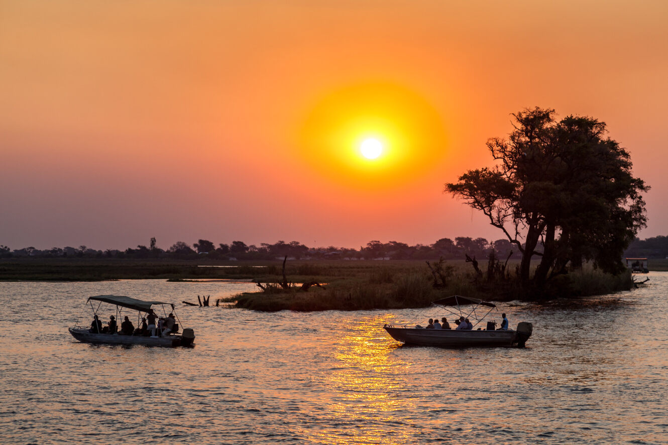 A couple of boats with people on sailing over a river in Botswana at sunset