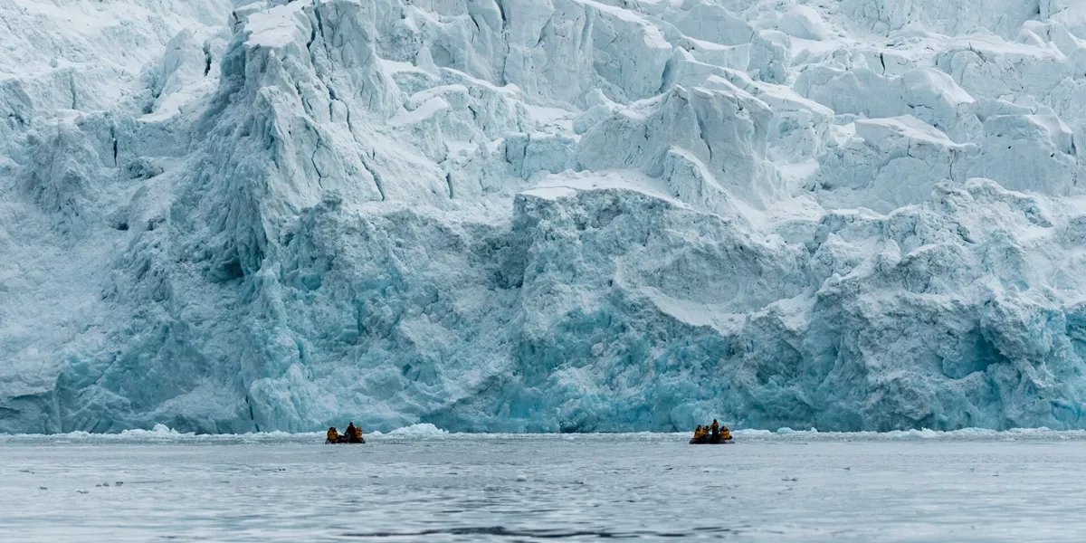 people on inflatable boats in front of a large glacier